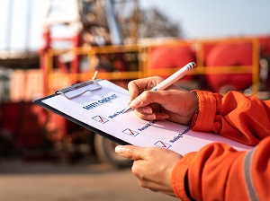 Industrial worker wearing safety orange is completing a checklist on a clipboard.