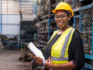 A shop worker wearing PPE is holding a clipboard.