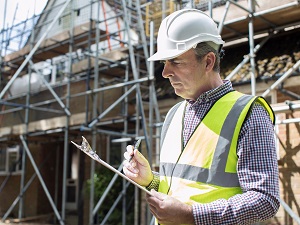 A construction supervisor is looking at a checklist on a clipboard.