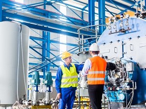 A supervisor is interviewing a shop worker standing next to heavy machinery.