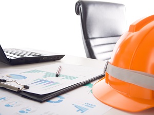 Graphs of data on a clipboard with a hardhat and laptop computer nearby.