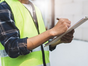 A worker wearing a safety vest using a clipboard to conduct a workplace inspection.