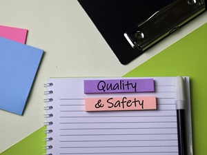 Office products on a desk with the words Quality and Safety written on post-it note tabs.