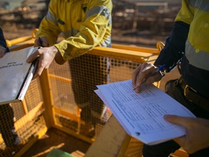 Workers in safety gear conducting an Activity Hazard Analysis (AHA) on a construction site, reviewing and writing on documents near safety barriers.