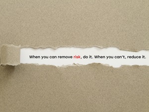 A piece of torn paper revealing the text underneath: "When you can remove risk, do it. When you can't, reduce it." The word "risk" is highlighted in red.