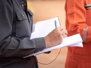 Person in work attire holding a notepad and pen, taking notes during an inspection or investigation.