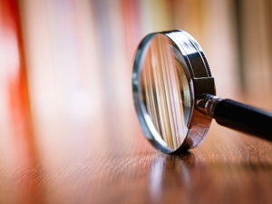 Close-up of a magnifying glass resting on a wooden surface, symbolizing investigation and scrutiny.