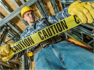 A construction worker in safety gear holding yellow caution tape inside a building under construction.