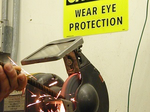 Worker Using Grinder with Caution Sign Above That Says Wear Eye Protection