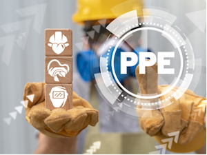 A construction worker wearing gloves holds three wooden blocks showing icons for hard hats, gloves, and safety goggles, with the word “PPE” displayed digitally in front.