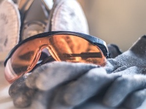 Amber-tinted safety glasses placed on top of protective gloves with a respirator in the background.