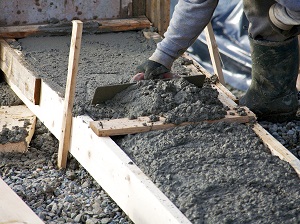 Worker wearing gloves spreading out wet concrete during construction.