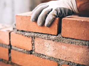 Worker wearing gloves building a brick wall with mortar.