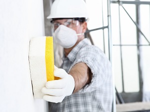 Construction Worker Wearing Face Mask and Gloves is Wiping Wall with Sponge