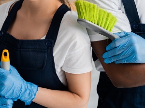 Two workers wearing gloves and holding cleaning tools standing side by side as they prepare to start cleaning.