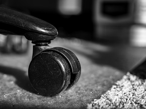 A close-up view of an office chair wheel sitting on a mat that is on a carpet.