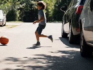 A young child chasing a ball running into the street from between two cars.