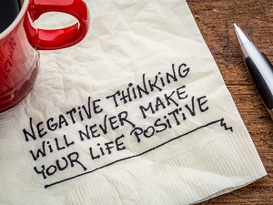 A cup of coffee next to a napkin that someone has written these words, "Negative thinking will never make your life positive."