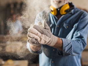 A woodworker wearing gloves clapping hands together to show there is a lot of dust in the air.