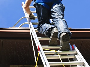 A worker safely climbing an extension ladder to get onto a roof.