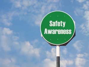 A round green sign against a blue sky with clouds that says, "Safety Awareness."