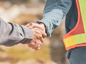 Two people shaking hands, one is wearing a safety vest.