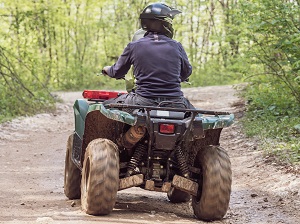 Driver on an all-terrain vehicle, rear view, on dirt path.