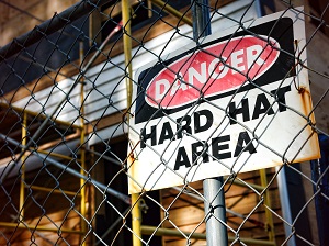 Construction site behind a fence with a sign that says Danger, Hard Hat Area.