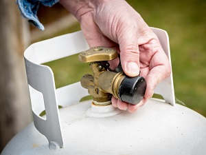 A person's hand opening the nozzle on a smaller propane tank.