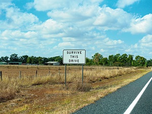 A stretch of highway with a sign on the side of the road that says "Survive This Drive."