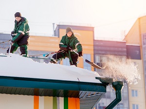 Two workers utilizing fall protection while removing snow from a rooftop.