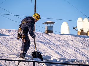 A worker removing snow from a roof using a shovel.
