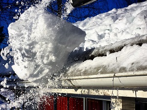 A large chunk of ice and snow falling off a roof that has been pushed off by a worker using a shovel.