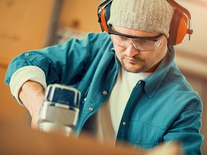 A worker wearing hearing protection and safety glasses using a nail gun.