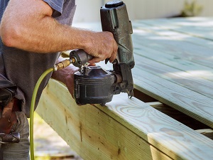 A worker using a nail gun while building a wooden deck.