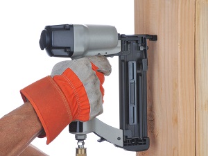 A worker's gloved hand using a nail gun.