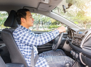 A man in a flannel shirt driving a car while sitting with good posture.