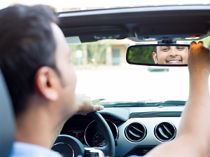 A smiling man looking into the rearview mirror as he sits in the driver's seat of his car.