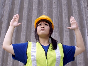 A worker wearing a hard hat and a safety vest using hand signals.
