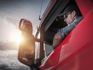 A truck driver looking into the side mirror.