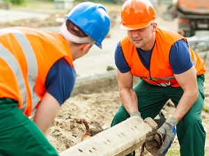 Two construction workers lifting a heavy block on site.