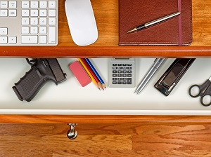 A desk drawer that has office supplies and a visible handgun.