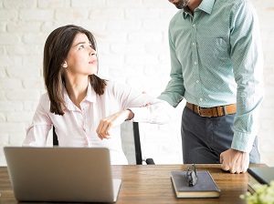 A standing worker forcibly grabbing another worker's arm who is seated.