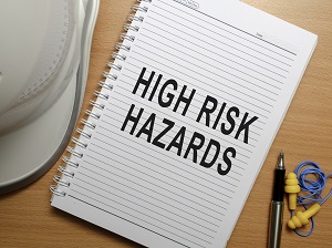 Hardhat and earplugs on a desk next to a notepad that says High Risk Hazards.