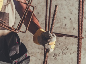 Construction worker holding rebar while wearing gloves and a tool belt.