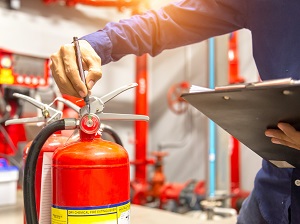 An inspector with a clipboard inspecting a fire extinguisher.