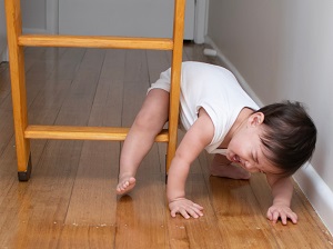 A crying baby stuck on the bottom rung of a ladder set up inside a house.