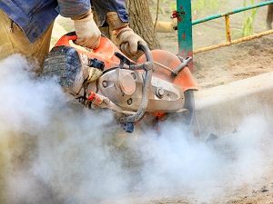 Worker using a handheld power saw that is producing sparks and a lot of visible dust.