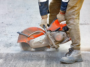 Worker using a handheld power saw to cut into the concrete road.