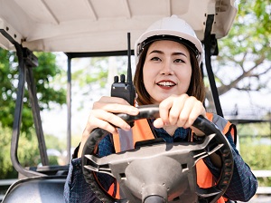 Smiling woman wearing PPE while driving a golf cart.